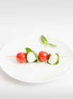 Bocconcini, cherry tomatoes and basil leaves skewer on a white plate