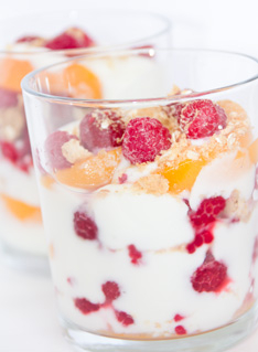 Fruity breakfast mix with vanilla yoghurt, raspberries, peaches and muesli in a glass