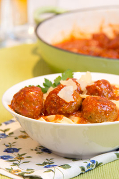 Easy family dinner recipe, homemade meatballs with pasta and parmesan in a white bowl on a flowerry blue and green tablecloth with green pan on the background