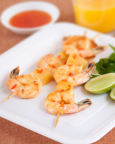 party food recipe of Lime and Chilli Prawns Skewers on a white plate with lime wedges with the dipping sauce and orange juice at the background
